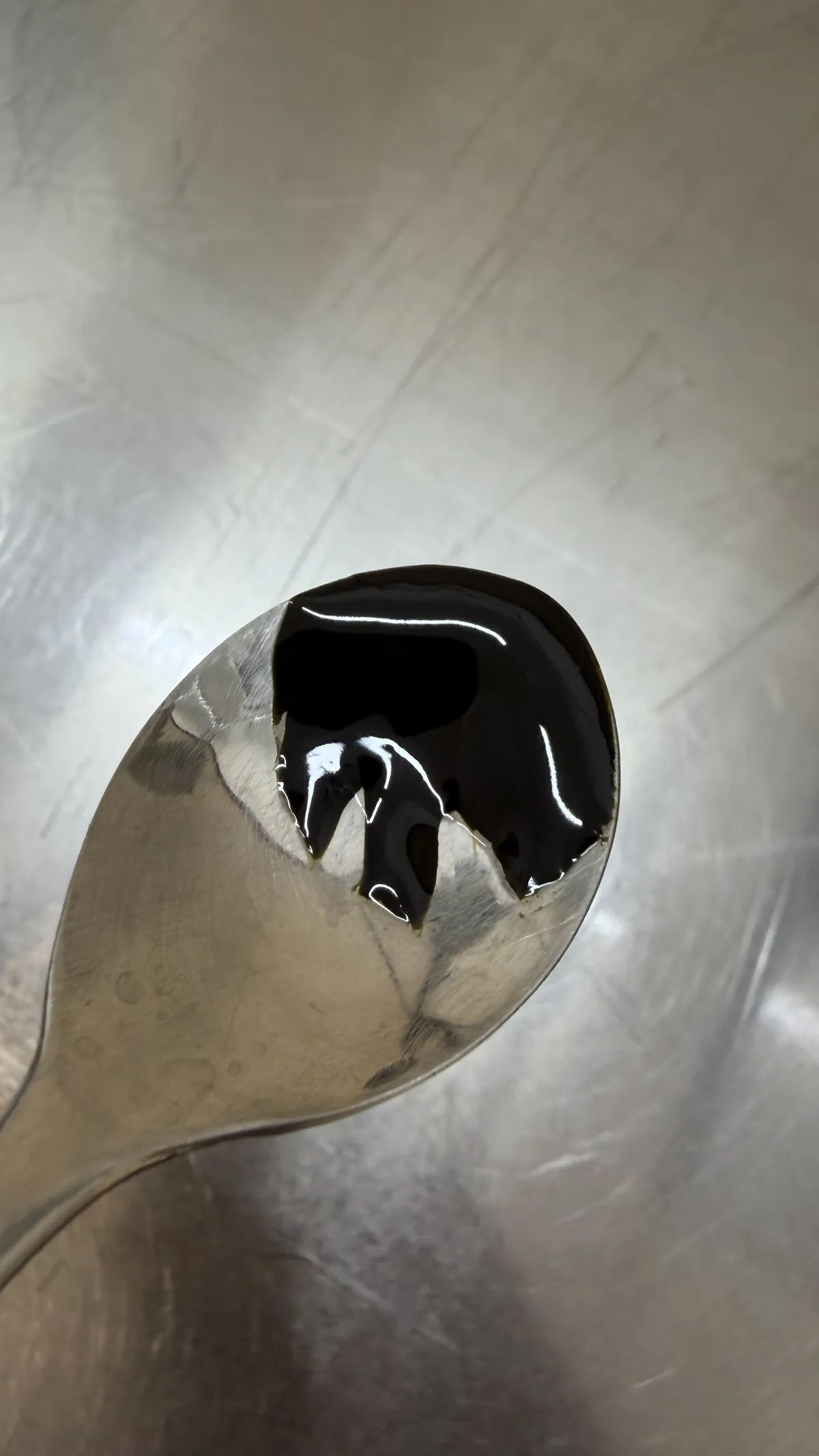 Dense shiny spruce bud resin on a spoon — consistency at the technological limit of solubility